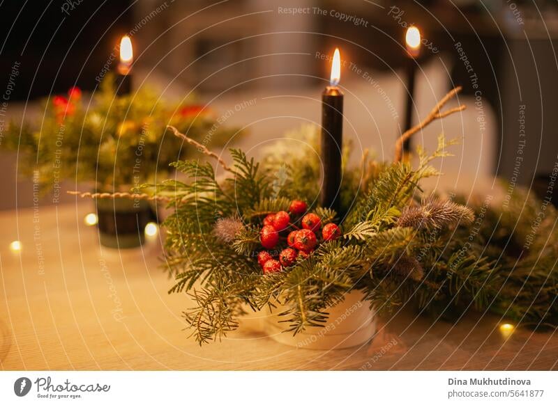 Weihnachtliches Blumenarrangement mit brennender Kerze. Mittelstück festliche Dekoration mit Nadelbaumzweigen und Beeren. Weihnachten geblümt Ordnung Kerzen