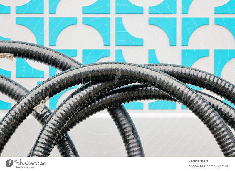 Schwarze Schläuche in Kurven vor blauem Wandmuster Schlauch schwarz Muster abstrakt Kontrast hellblau Baumaterialien Baustelle Kunst Installation Textur Konzept