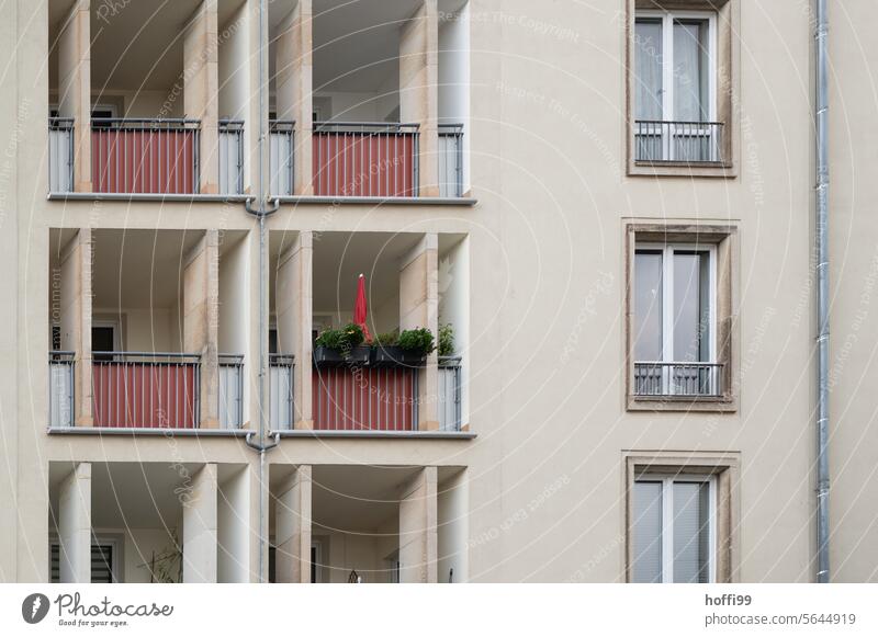 graue Wohnhausfassade mit roten Balkonen und einem eingeklappten roten Sonnenschirm Mietskaserne 60er Jahre bedeckt Tristesse trist Fassade Gebäude urban