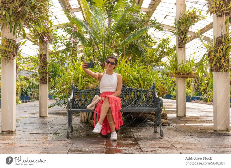 Frau, die ein Selfie mit dem Handy auf einer Bank im Botanischen Garten macht chapultepec Jardi Botanic Smartphone Gewächshaus Funktelefon Mexiko Tourist