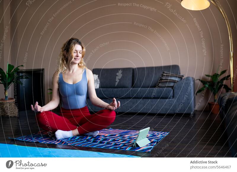 Junge Frau übt Yoga zu Hause auf einer Matte heimwärts Unterlage praktizieren Smartphone Pose Gelassenheit farbenfroh gemütlich Wohnzimmer Fitness Wohlbefinden