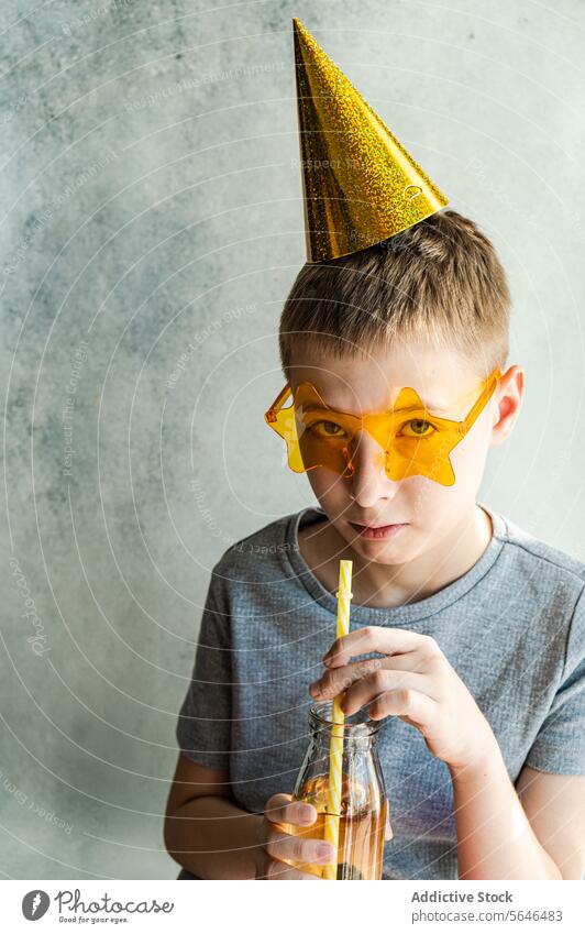 Junge mit Partyhut und sternförmigen Gläsern nippt an einem Getränk Neujahrsfest sternförmige Gläser trinken Glasflasche Stroh Geburtstag Feier glitzernd gelb