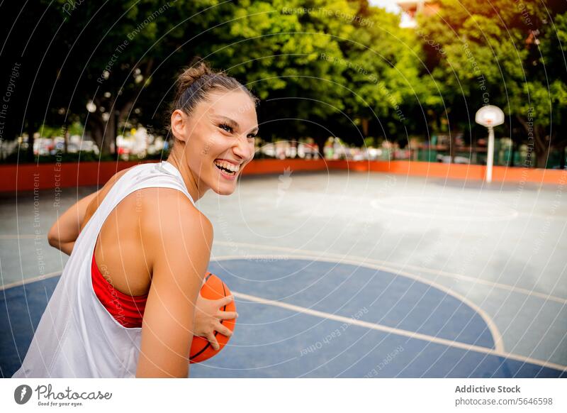 Lachende Frau, die tagsüber auf einem Platz Basketball spielt Sportlerin spielen Ball Spieler heiter Training genießen Spielplatz Lächeln Aktivität Glück Sommer