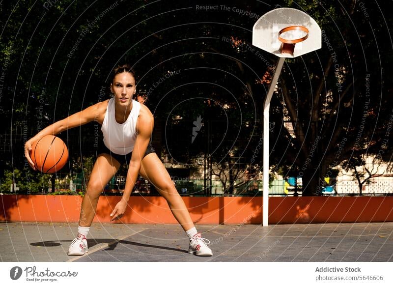 Sportliche junge Frau in Sportkleidung schaut in die Kamera, während sie an einem sonnigen Sommertag Basketball spielt. Sportlerin spielen Gericht dribbeln