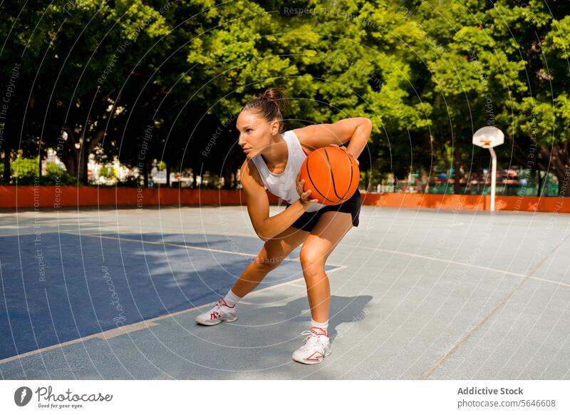 Ganzer Körper einer sportlichen jungen Frau in Sportkleidung, die wegschaut, während sie an einem sonnigen Sommertag auf dem Platz Basketball spielt Sportlerin
