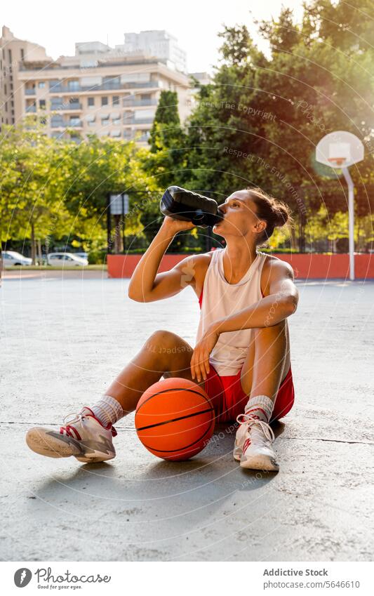 Sportlerin trinkt Wasser nach dem Basketballspiel auf dem Platz trinken Flasche Spieler Sportpark Ball ruhen Hydrat Frau Spielplatz Großstadt jung Erfrischung