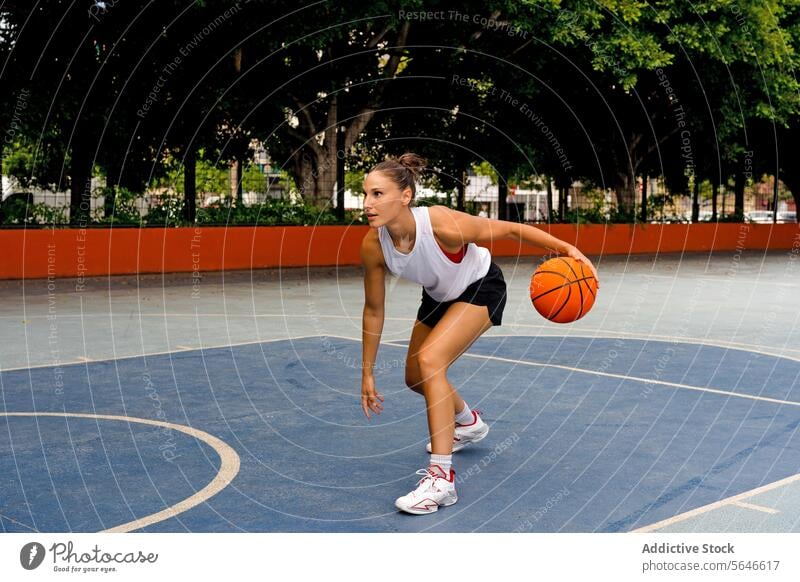 Ganzkörper-Seitenansicht einer sportlichen jungen Frau in Activewear, die beim Basketballspielen auf einem Platz an einem sonnigen Sommertag wegschaut