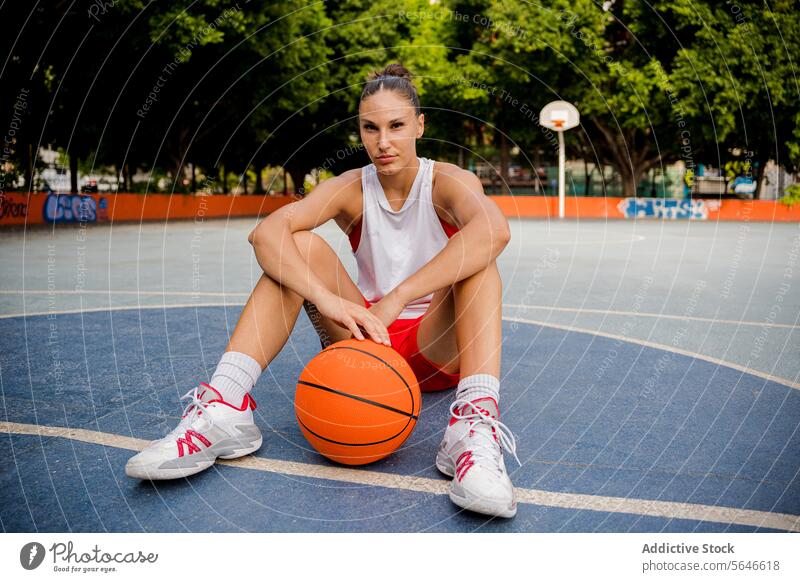 Selbstbewusste Frau sitzt mit Basketball auf einem Spielplatz Sportlerin Ball selbstbewusst Gericht sportlich Spieler sich[Akk] entspannen Athlet Sportpark