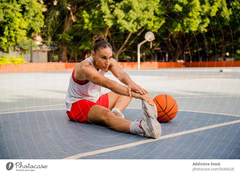 Frau streckt die Beine vor dem Basketballspiel auf dem Platz Sportlerin Spieler Aufwärmen Dehnung Übung Fuß Sportpark Training Bestimmen Sie Spielplatz jung
