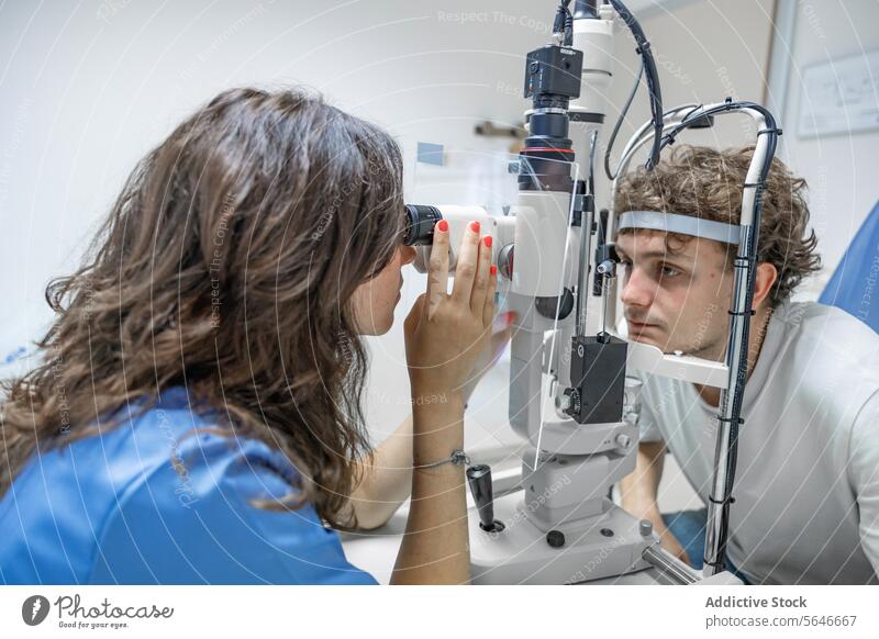 Junge Ärztin untersucht das Auge eines unkenntlichen Mannes in einer Klinik in Lichtern Frau Arzt geduldig Uniform Stethoskop prüfen Spaltlampen-Biomikroskop