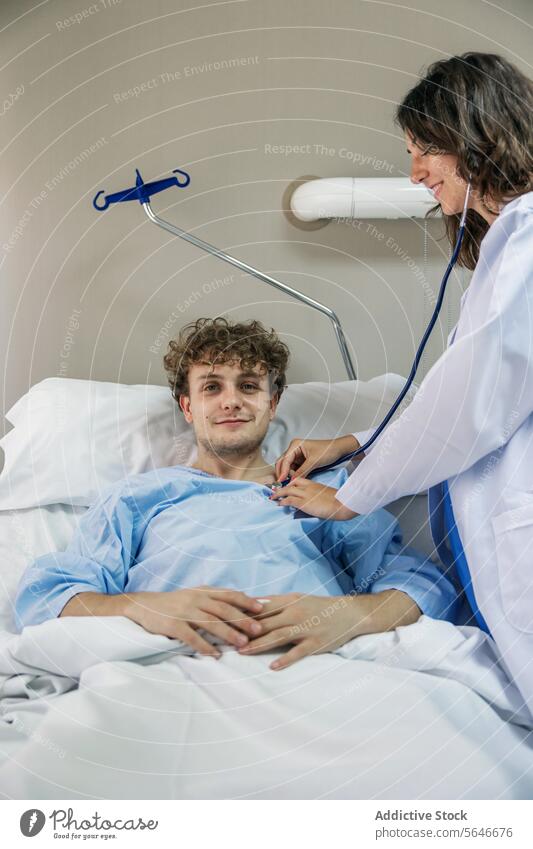 Arzt, der einen auf dem Bett liegenden Patienten mit einem Stethoskop in einer Klinik untersucht Mann geduldig Lächeln Glück Krankenpfleger prüfen untersuchen