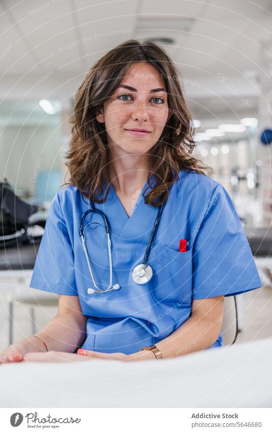 Glückliche junge Ärztin in Uniform sitzt am Tisch im Krankenhaus Frau Porträt Arzt Lächeln professionell Stethoskop Arbeit Gesundheitswesen Job sitzen