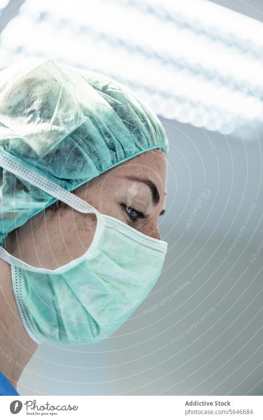 Ärztin mit Schutzmaske und Kappe schaut auf ein Krankenhaus hinunter Frau Mundschutz Chirurg Arzt Klinik behüten Uniform Gesundheitswesen Verschlussdeckel