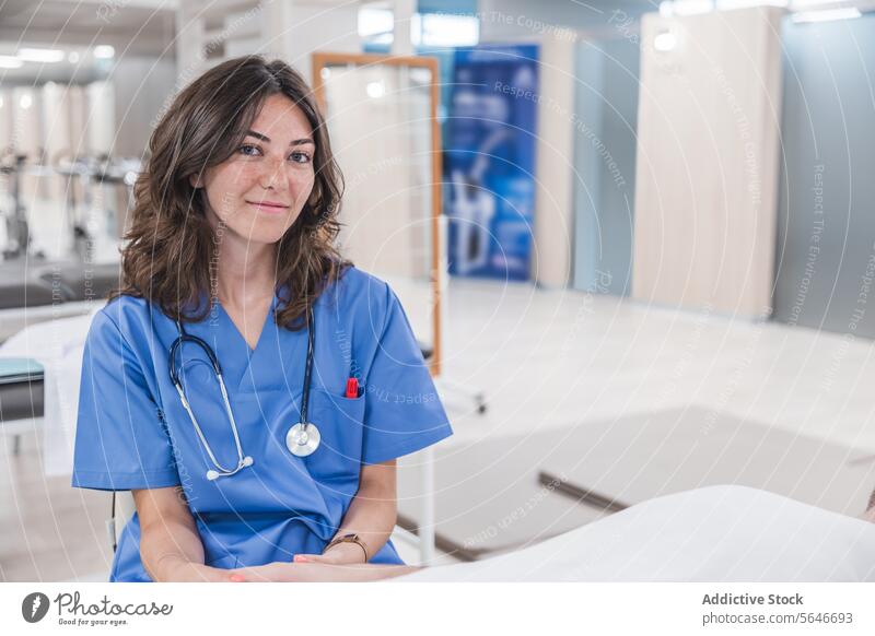 Glückliche junge Ärztin in Uniform sitzt am Tisch im Krankenhaus Frau Arzt Lächeln professionell Stethoskop Arbeit Gesundheitswesen Job sitzen Schreibstift