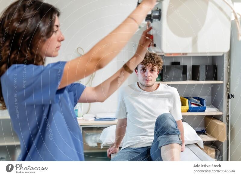 Junge Technikerin justiert Röntgengerät zum Scannen eines Patienten, der auf einem Bett in einer Klinik sitzt Frau Krankenpfleger geduldig Mann Röntgenbild