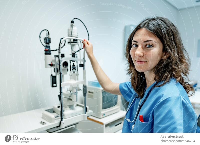 Glückliche junge Frau Arzt stehend neben Spaltlampe Biomikroskop im Krankenhaus Lächeln Uniform Stethoskop Spaltlampen-Biomikroskop leuchten Schreibstift