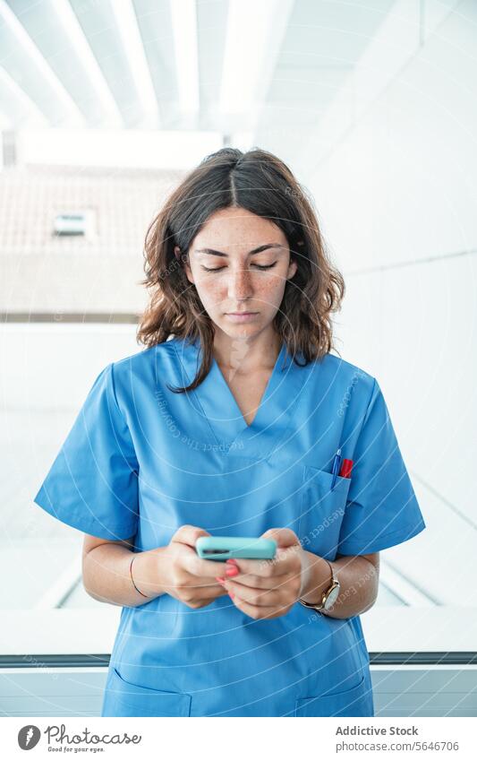 Junge Ärztin mit Mobiltelefon im Krankenhaus Frau Arzt Smartphone benutzend Browsen Klinik Krankenpfleger Uniform Surfen professionell Mobile Telefon Spezialist