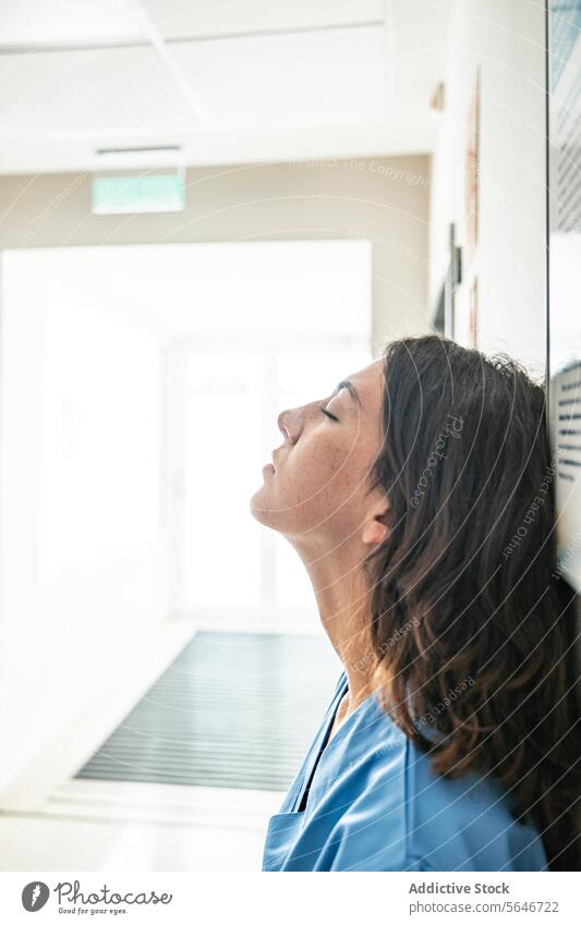 Junge Ärztin, die sich im Krankenhaus an die Wand lehnt Frau Arzt Augen geschlossen sich[Akk] entspannen Klinik Medizin Uniform fettarm krause Haare