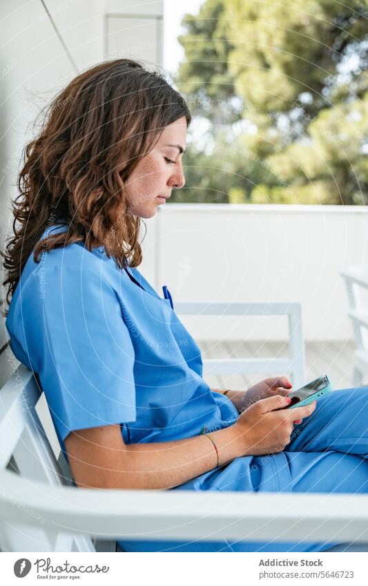 Junge Krankenschwester, die auf einer Bank sitzend auf ihrem Smartphone surft Frau Krankenpfleger Krankenhaus benutzend Browsen Uniform Medizin