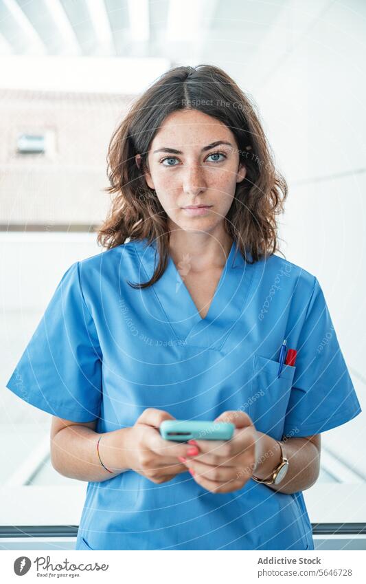 Junge Ärztin mit Mobiltelefon im Krankenhaus Frau Arzt Porträt Smartphone benutzend Browsen Klinik Krankenpfleger Uniform Surfen professionell Mobile Telefon