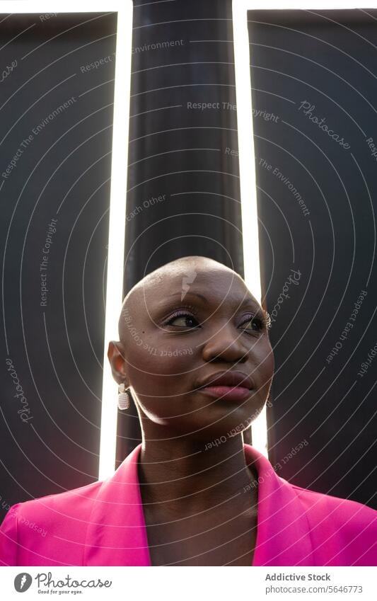 Selbstbewusste schwarze Frau mit rasiertem Kopf in rosa Outfit steht vor einem Rahmen mit Lichtern selbstbewusst Wand Individualität Vorschein rasierter Kopf