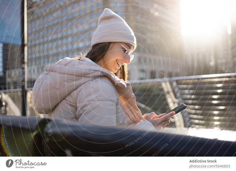 Glückliche Frau in warmer Kleidung beim Telefonieren in der Stadt Tourist benutzend Smartphone Lächeln Browsen Großstadt Ausflug Urlaub Mobile jung Hut heiter