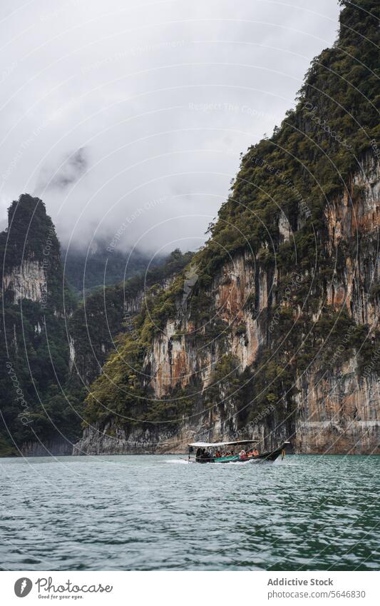Boot schwimmt auf einem kräuselnden See in der Nähe hoher Berge in Thailand Menschen Tourist reisen Berge u. Gebirge felsig Natur Cloud Grün Cheow Lan See Asien