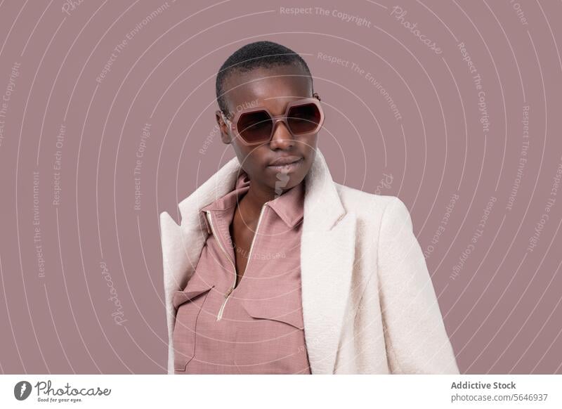 Nachdenkliches junges kühnes afroamerikanisches weibliches Modell in trendigem Outfit und Sonnenbrille, das auf rosa Hintergrund wegschaut Frau trendy Stil