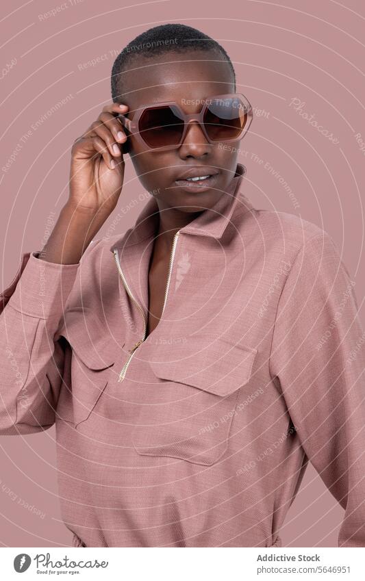 Junges kühnes afroamerikanisches weibliches Modell in stilvoller rosa Kleidung und Sonnenbrille stehend und wegschauend vor rosa Hintergrund Frau Stil trendy