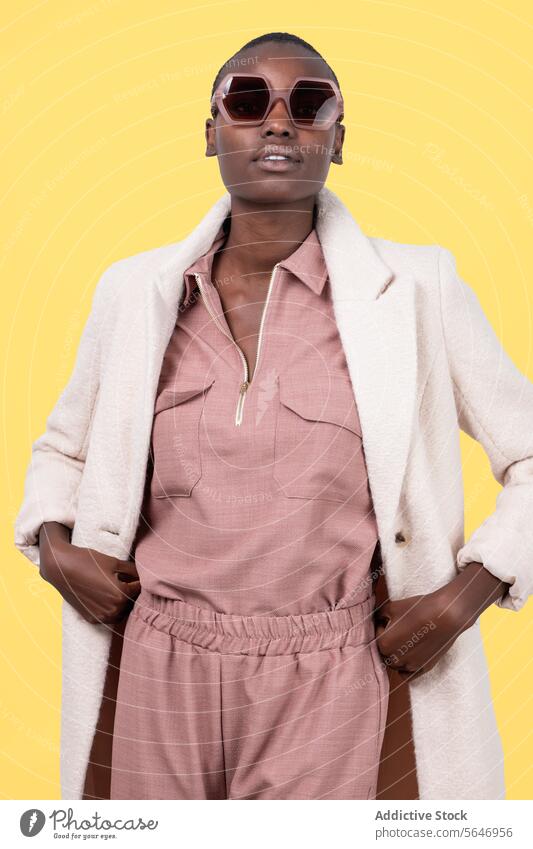 Nachdenkliches junges kühnes afroamerikanisches weibliches Modell in trendigem Outfit und Sonnenbrille schaut in die Kamera auf gelbem Hintergrund Frau trendy