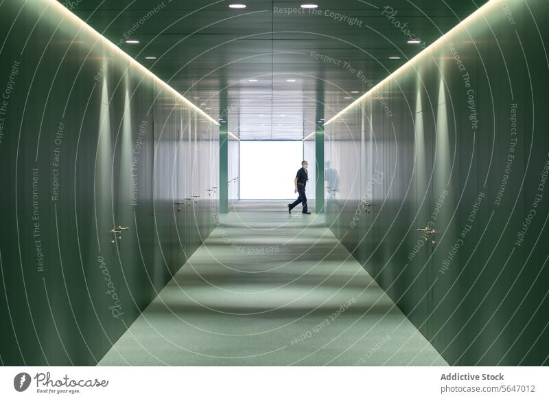 Seitenansicht eines anonymen Mannes, der durch einen beleuchteten Gang mit grünen Wänden in einem modernen Krankenhaus geht Durchgang Zimmerdecke Licht
