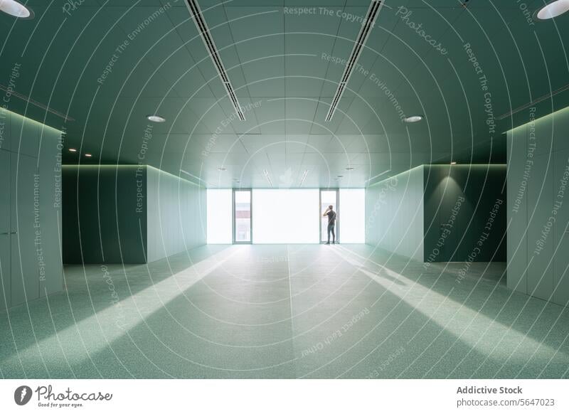 Anonymer Mann mit Smartphone in einem leeren grünen Raum mit Glastüren in einem modernen Krankenhaus stehend Tür Wand Zimmerdecke Innenbereich medizinisch