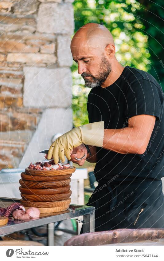 Fokussierter Koch in Handschuhen beim Schneiden von Oktopus auf Holztellern in Galicien Küchenchef Octopus Galicia Holzplatte traditionell Speise Konzentration