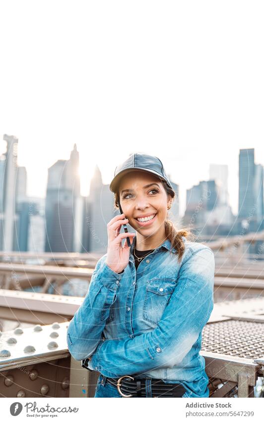 Frau chattet am Telefon mit Blick auf Manhattan Anruf Sonnenbrille Skyline Stadtbild New York State Gespräch urban Brücke Mode Freude Jeansstoff glühen