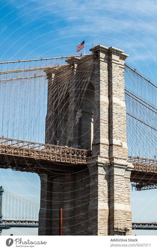 Turm der Brooklyn Bridge mit wehender amerikanischer Flagge vor blauem Himmel. Brücke Amerikaner Fahne Architektur kultig Wahrzeichen New York State Kabel Stein
