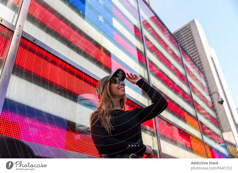 Stylische Frau vor digitaler amerikanischer Flagge am Times Square Stil Sonnenbrille Lächeln Bildschirm Fahne Amerikaner Manhattan New York State pulsierend