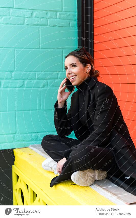 Junge Frau sitzt auf einer Mauer und spricht mit ihrem Smartphone reden Telefonanruf sprechen Lächeln Glück Straße Gespräch heiter jung Mobile Kleid Gerät