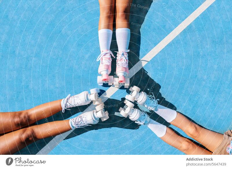 Crop junge Freundinnen mit Rollschuhbeinen treffen sich auf dem Sportplatz Frauen Dehnung Rolle Bein Radialsymmetrie Zusammensein Rollerskate Aktivität schwarz