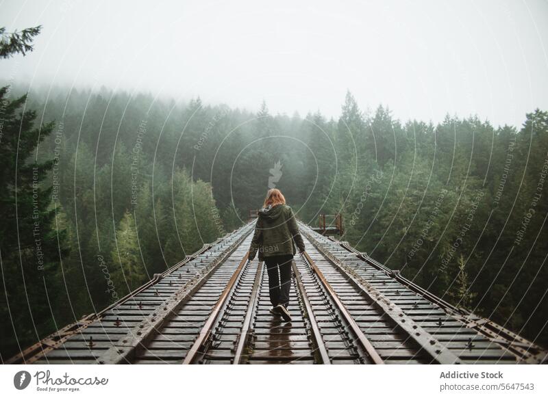 Frau spaziert in nebliger Waldschneise auf Vancouver Island Person Spaziergang Eisenbahn Nebel Abenteuer Mysterium Rückansicht British Columbia Kanada Grün
