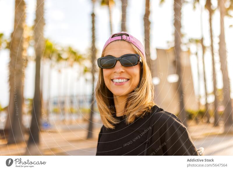 Glückliche schöne Frau mit blondem Haar Sonnenbrille Verschlussdeckel Porträt Lächeln T-Shirt attraktiv schwarz rosa Park Behaarung Unschärfe genießen
