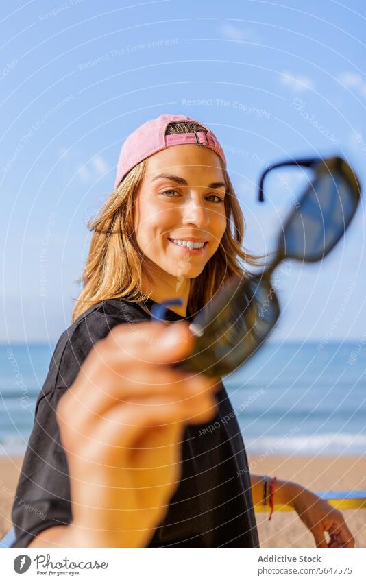 Lächelnde Frau am Meer im Sommer Glück Sonnenbrille Verschlussdeckel zeigend Porträt Strand Himmel sonnig Lifestyle in die Kamera schauen stylisch blond