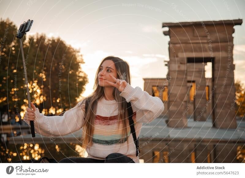 Junge Frau hält den Sonnenuntergang mit einem Selfie-Stick im Debod-Tempel in Madrid fest kleben Debütantin Einbeinstativ goldene Stunde historisch Hintergrund