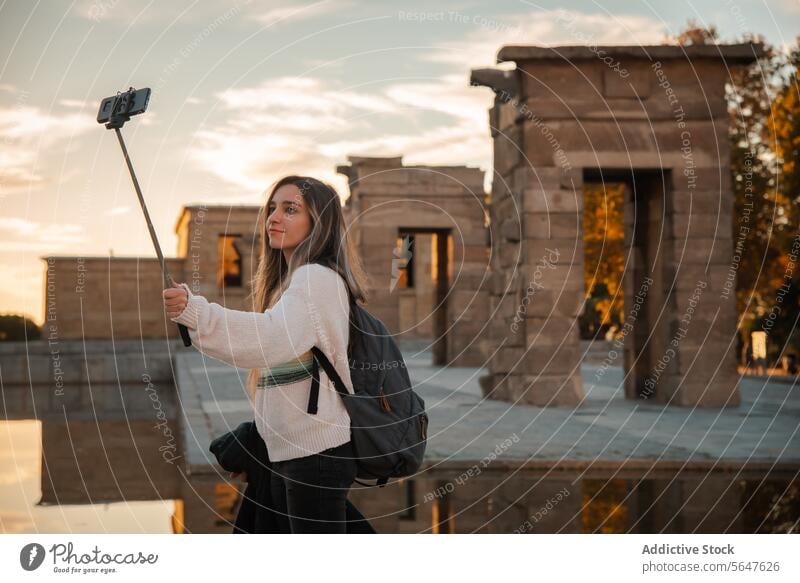 Junger Reisender macht ein Selfie im historischen Debod-Tempel in Madrid Frau Debütantin historische Stätte Sonnenuntergang Telefon Selfie-Stick Rucksack