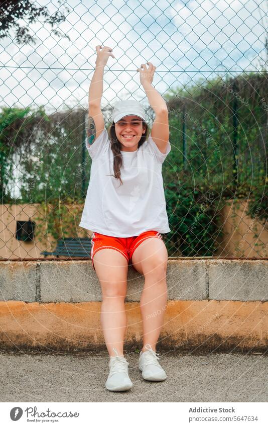 Fröhliche junge Frau während einer Trainingspause im Freien Freude Fröhlichkeit sportlich Kleidung Sitzen Seitenstreifen Laubwerk Hintergrund heiter lässig