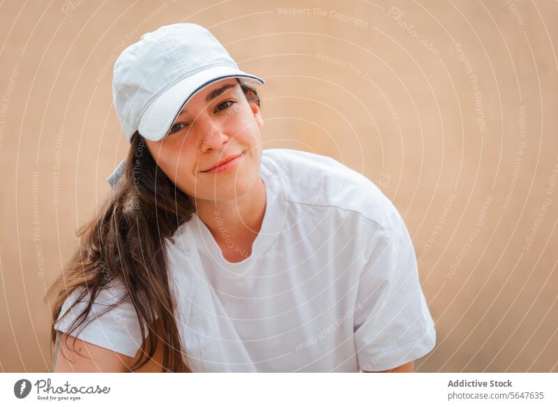 Lässig lächelnde Frau mit weißer Mütze und Hemd Lächeln lässig Verschlussdeckel jung entspannt beige in die Kamera schauen Hintergrund Lifestyle Porträt Mode
