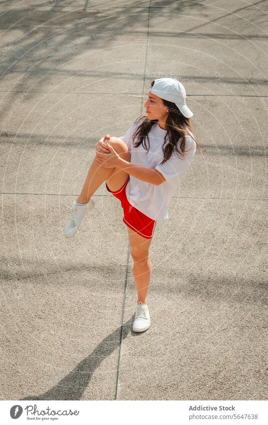 Aktive Frau beim Dehnen im Freien an einem sonnigen Tag strecken Sportbekleidung Verschlussdeckel rot Shorts Training Fitness Bein Straße tagsüber aktiv