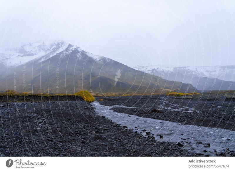 Neblige isländische Landschaft mit Bergen und Bach Island Berge u. Gebirge strömen ruhig Nebel verhüllt schwarzer Kieselstein Hintergrund Natur im Freien