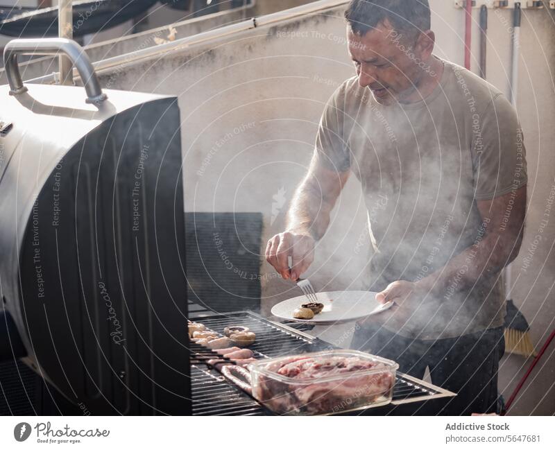 Männlicher Koch grillt Pilze und Fleisch auf einem Grillrost Mann Küchenchef Barbecue Wurstwaren Rauch lecker vorbereiten männlich Erwachsener stehen