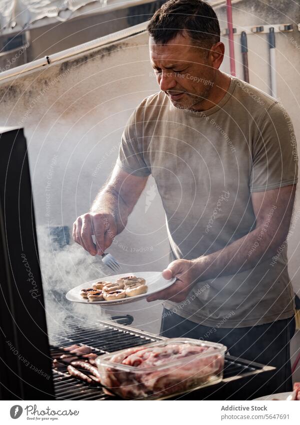Männlicher Koch grillt Pilze und Fleisch auf einem Grillrost Mann Küchenchef Barbecue Wurstwaren Rauch lecker vorbereiten männlich Erwachsener stehen