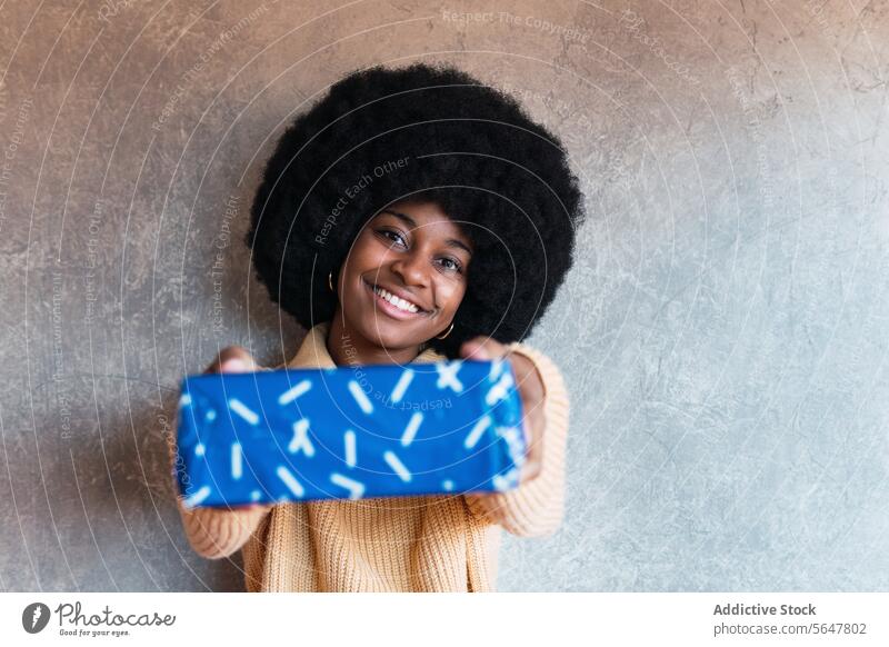 Lächelnde schwarze Frau überreicht Geschenk präsentieren umhüllen Kasten Feiertag Überraschung feiern geben Afroamerikaner Afro-Look heiter jung Glück